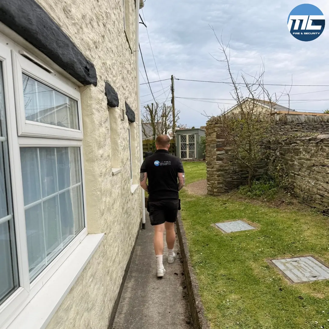 MC Fire & Security engineer walking up to a Cornwall stone-walled cottage on a fire alarm install