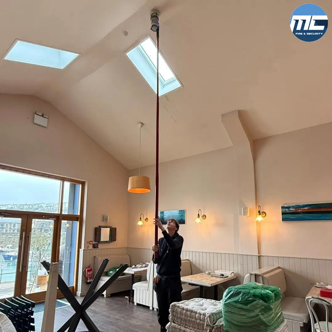 MC Fire & Security engineer testing a fire detector at height — Amélie Porthleven