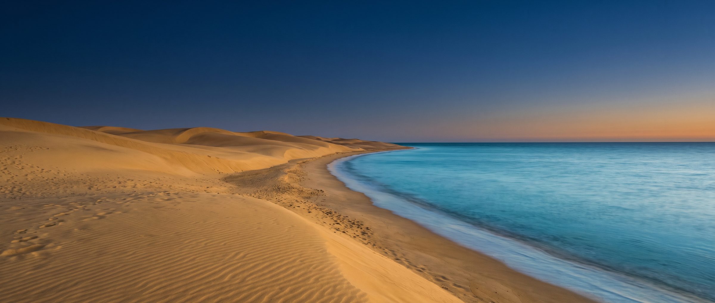 Golden dunes meeting a calm sea at blue hour