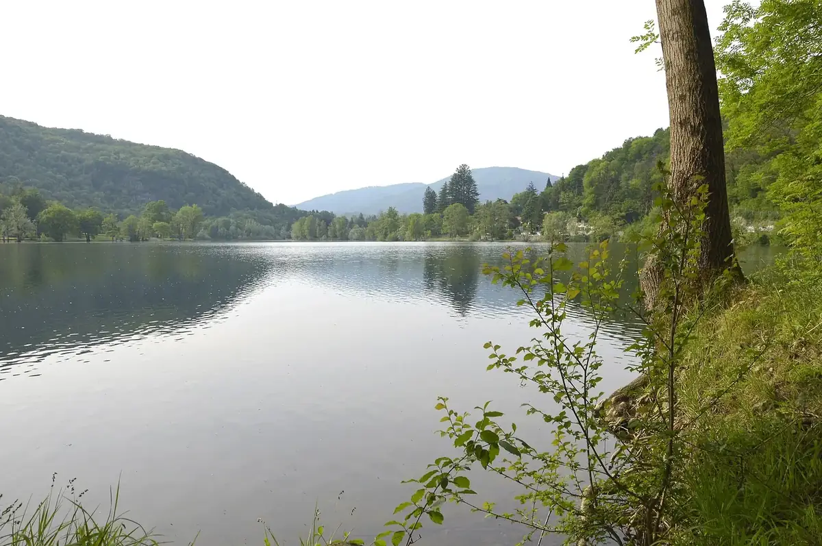 Veduta del Lago di Ganna dalla riva, con boschi e rilievi sullo sfondo.