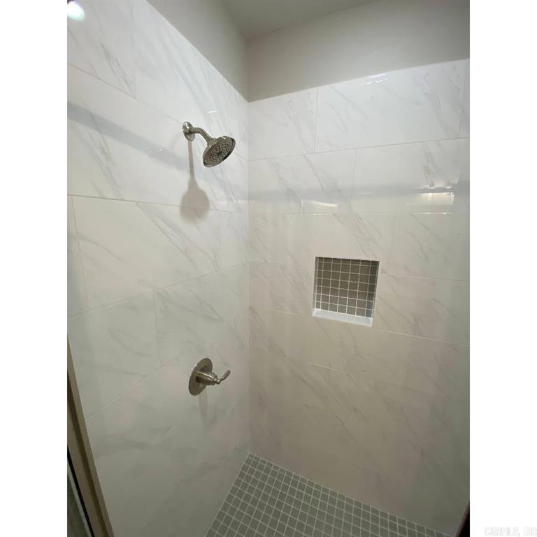 Primary bathroom shower with marble-look tile and inset niche