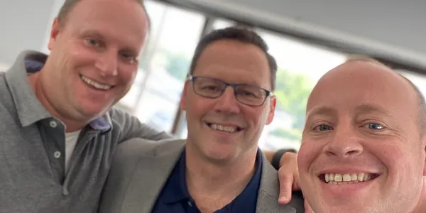 Three smiling men pictured together in the Bellia testimonial photograph.