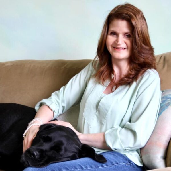 Jenna Galligani, founder of Holistic Awakenings, smiling with her dog Dory resting in her lap