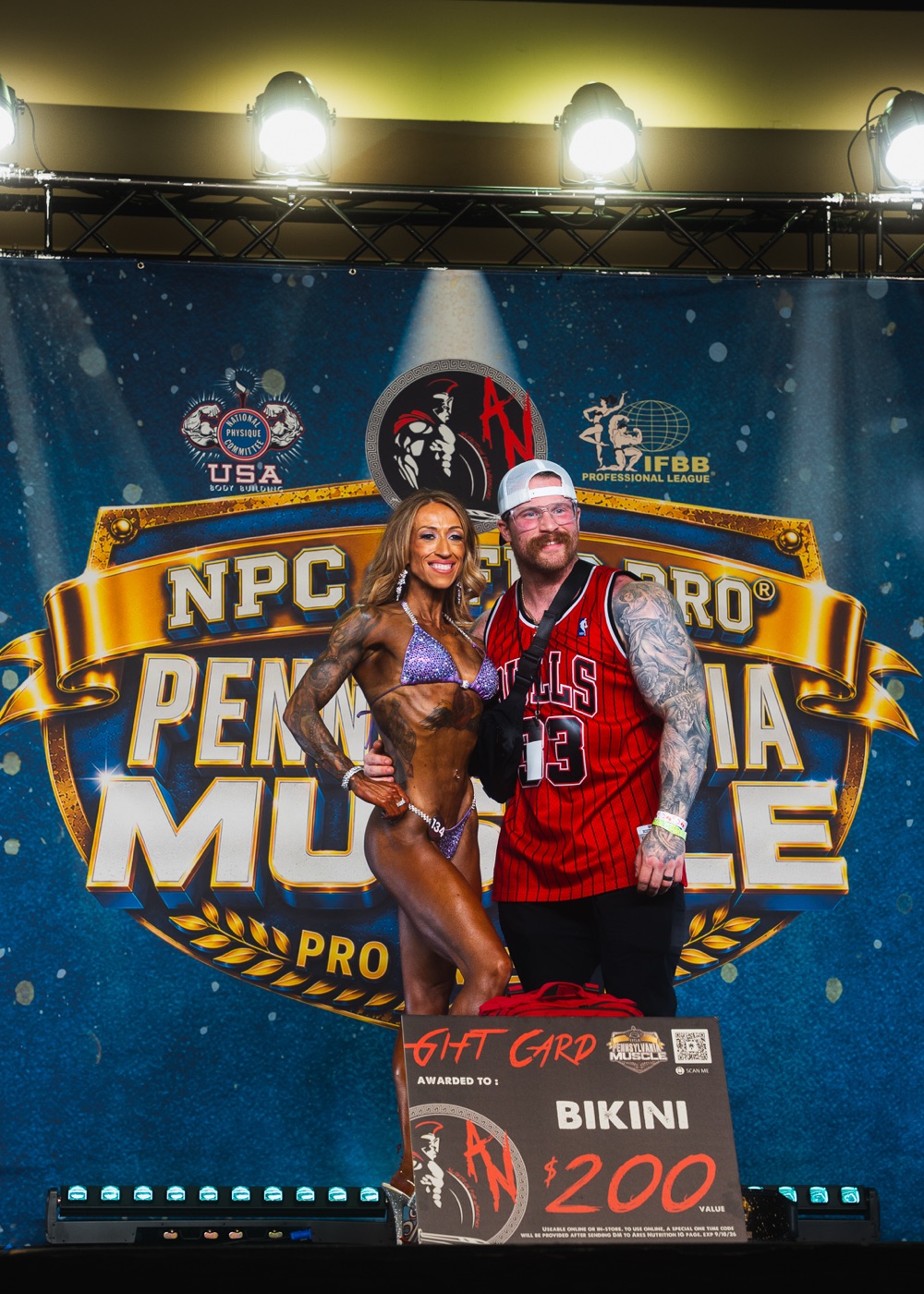 Asylum coach on stage with a bikini competition winner at NPC Pennsylvania Muscle Pro