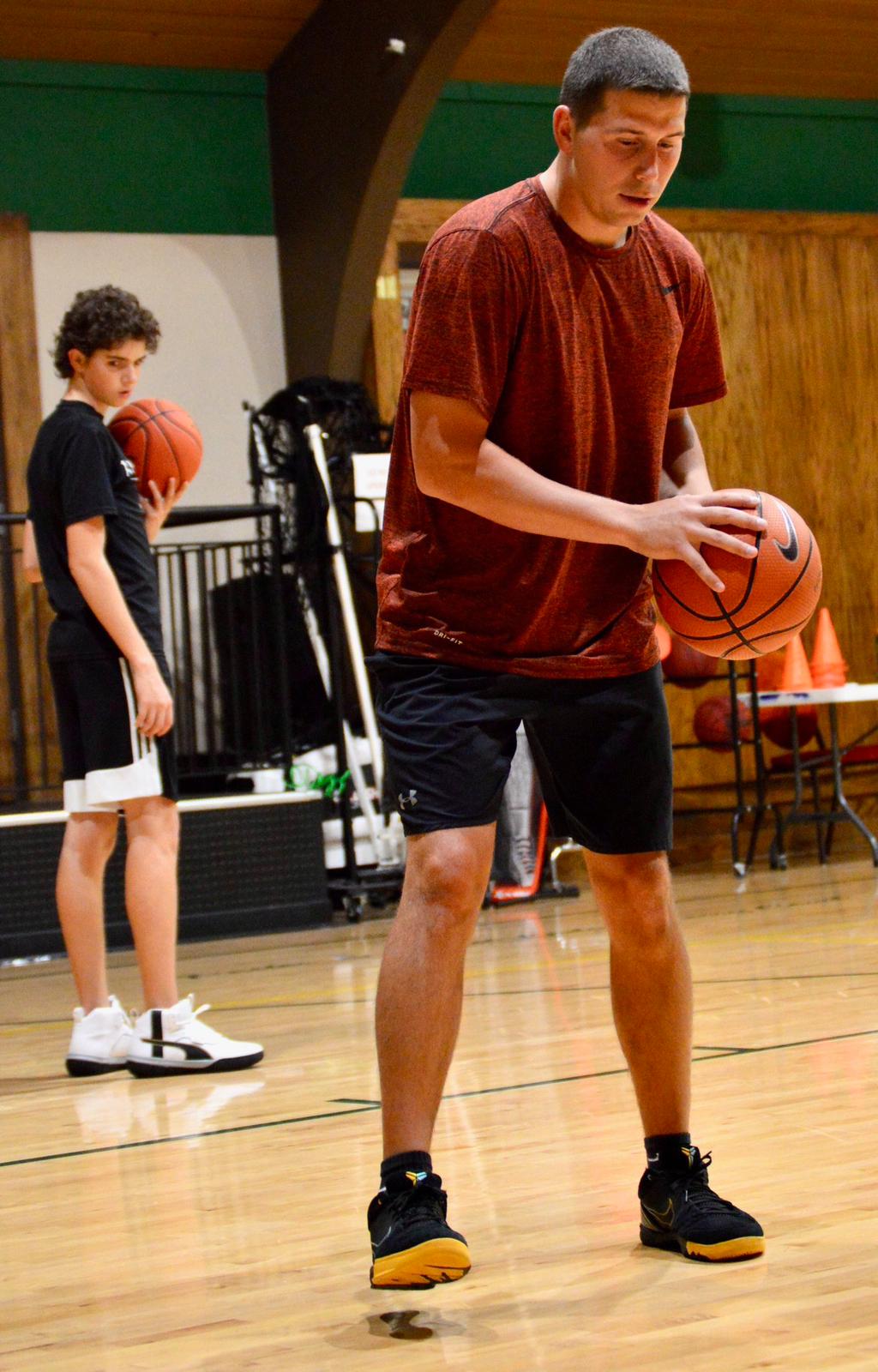 Basketball trainer Casey Teson demonstrating dribbling drills with a student during skills training session in the gym