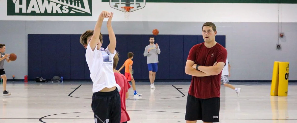 Young athlete practicing a jump shot while coach observes during basketball training.
