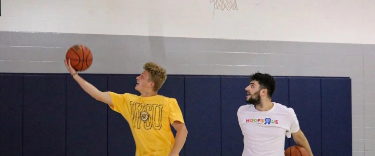 Youth player practicing a layup drill with a coach assisting during basketball practice.