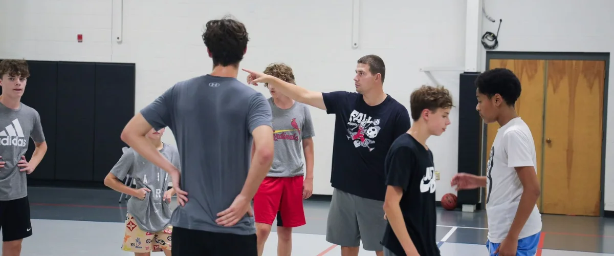 Coach giving instructions to teenage basketball players on gym court.
