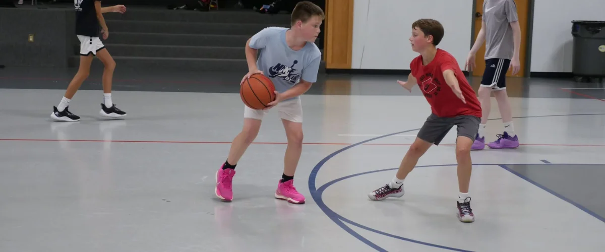 Youth basketball players practicing defense and ball handling indoors.