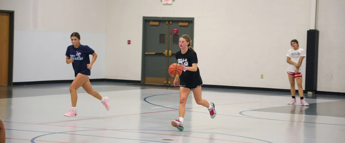 Girls practicing basketball dribbling during indoor training session.