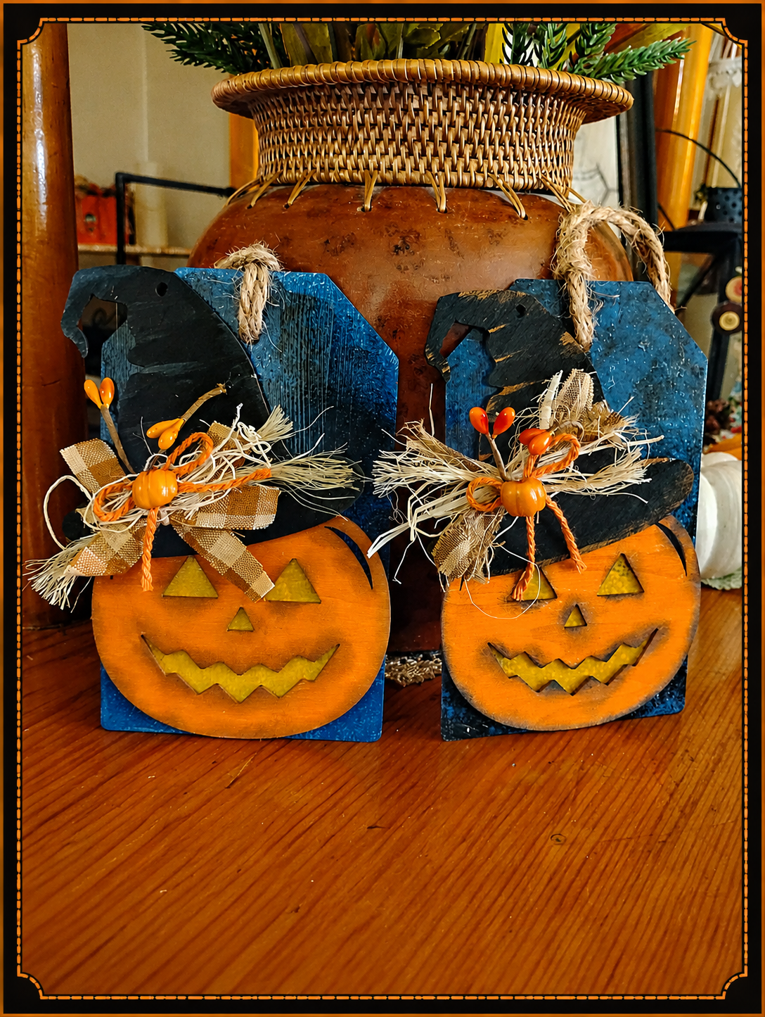 Two hand-painted wooden jack-o'-lanterns in witch hats, trimmed with burlap bows and raffia