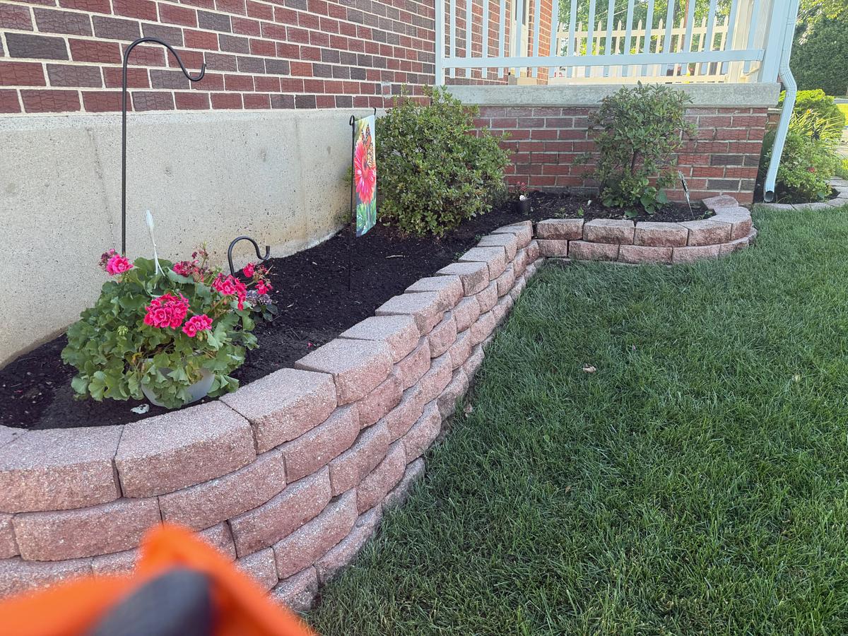 Segmental block retaining wall and planting bed washed clean, with pink geraniums in flower