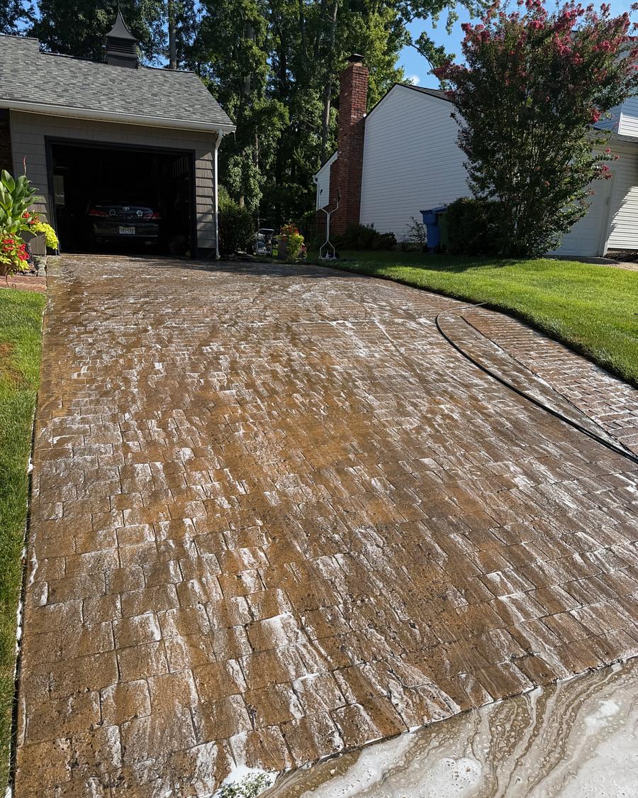 Stamped concrete driveway mid-wash, a sharp line between the cleaned section and the untouched dirty section
