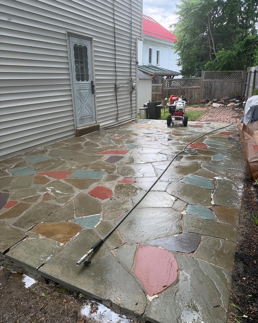 Washed multicolored flagstone patio with a pressure washing wand resting on the clean stone