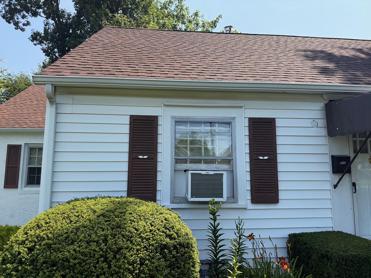 Corner of a washed white sided Havertown, PA home with a red shingle roof and clean white gutters