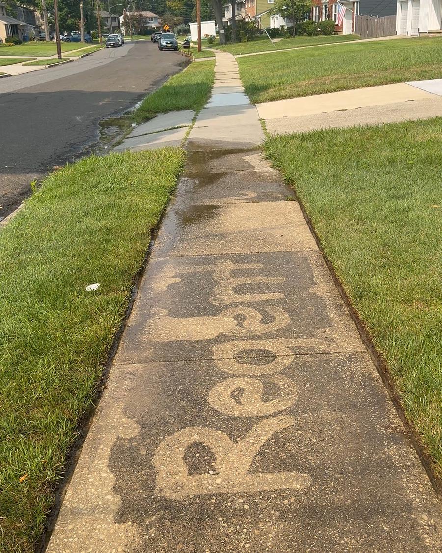 A concrete sidewalk with the word Regent cleaned into the surface, showing the contrast between washed and unwashed concrete