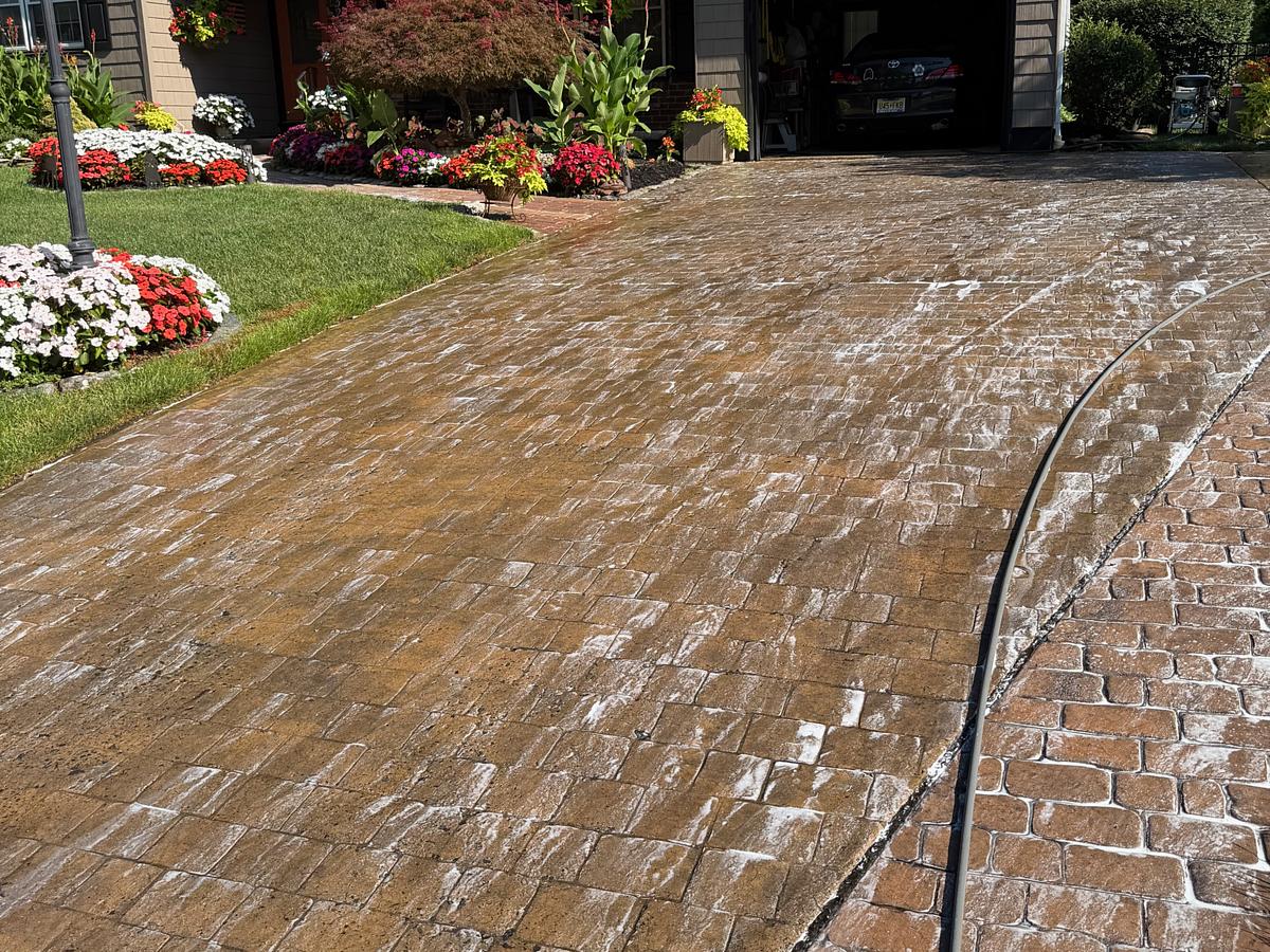 Surface cleaner passes across a stamped concrete driveway, foam and dirty run-off visible