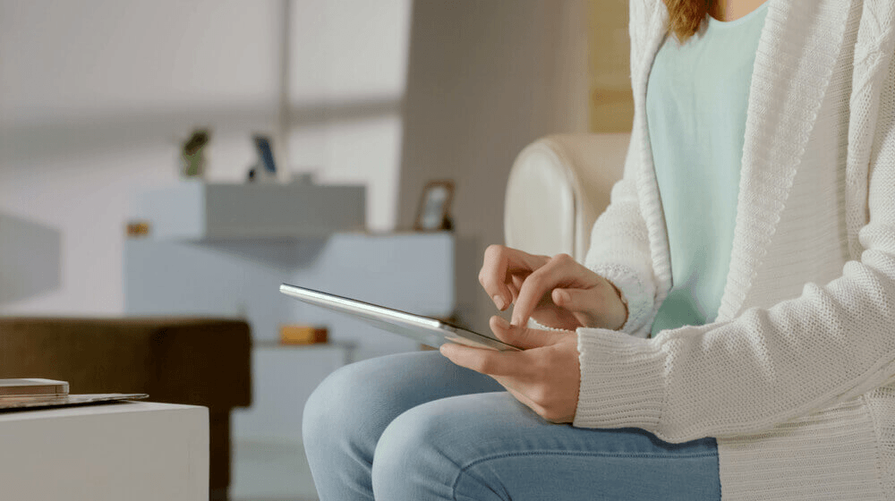 A person wearing a white cardigan and blue jeans researching MS diet information on a tablet while sitting on a couch.