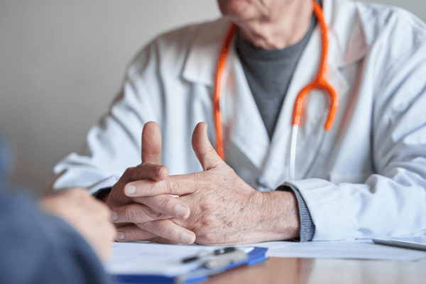 Doctor wearing a white coat and an orange stethoscope discussing MS and diet with a patient off-camera.