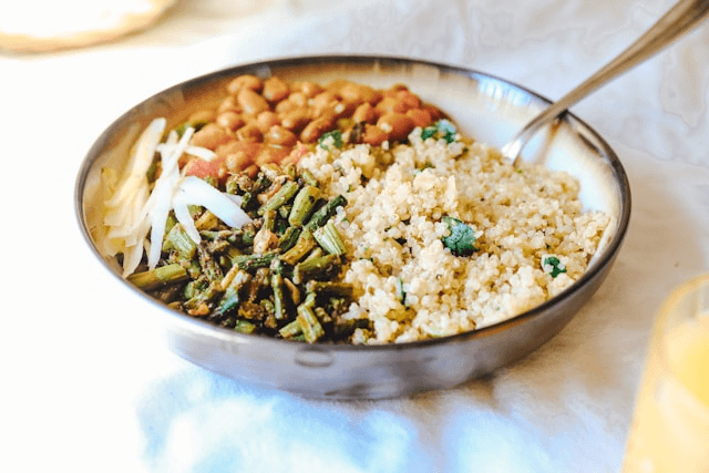 A close-up of a bowl filled with rice, beans, and chopped green vegetables, with a fork resting in the bowl.