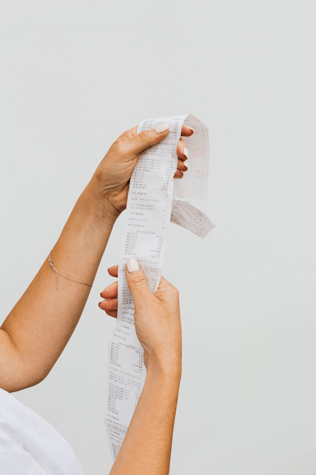 A long grocery receipt unfurling between two hands. A long grocery receipt unfurling between two hands.