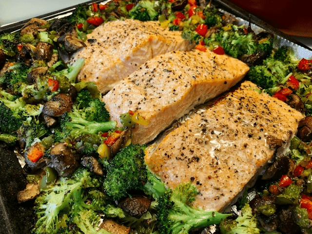 Three pieces of seasoned salmon fillet baked on a sheet pan with broccoli, mushrooms, and diced bell peppers. Three pieces of seasoned salmon fillet baked on a sheet pan with broccoli, mushrooms, and diced bell peppers.