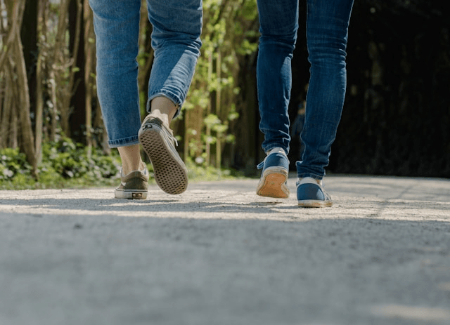 Two people walking on a path outdoors, wearing jeans and sneakers. Two people walking on a path outdoors, wearing jeans and sneakers.