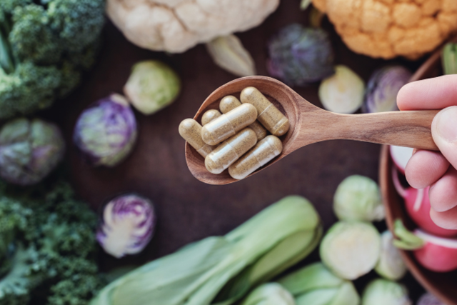 Supplement capsules on a wooden spoon surrounded by fresh vegetables, representing nutrient support for MS fatigue