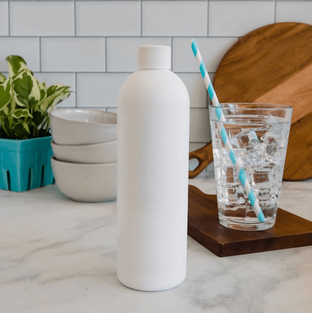 Plain white reusable bottle on a kitchen counter next to a glass of ice water with a striped straw.