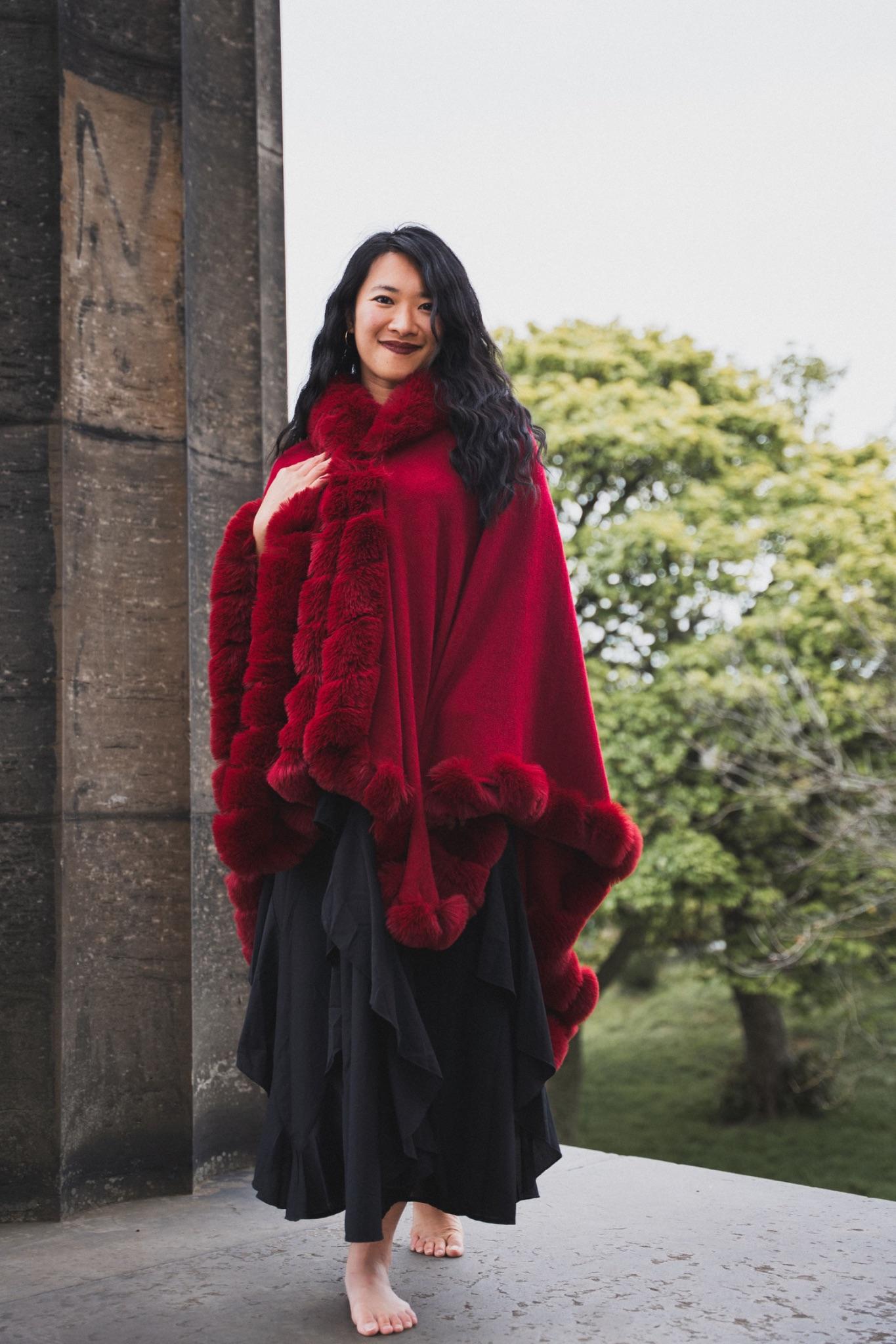 Mistress Mahara standing in a red fur cape between stone columns