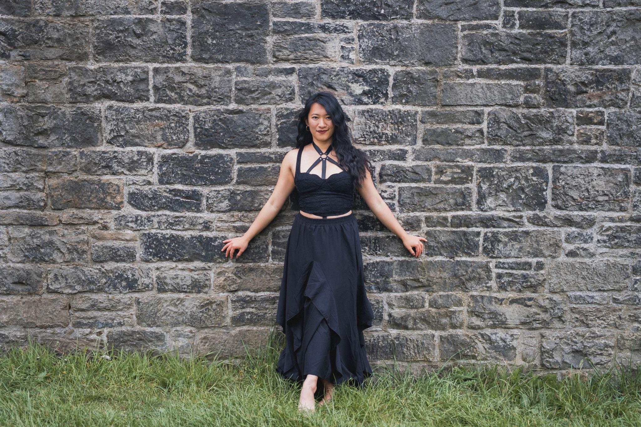 Mistress Mahara in a black gown against a stone wall