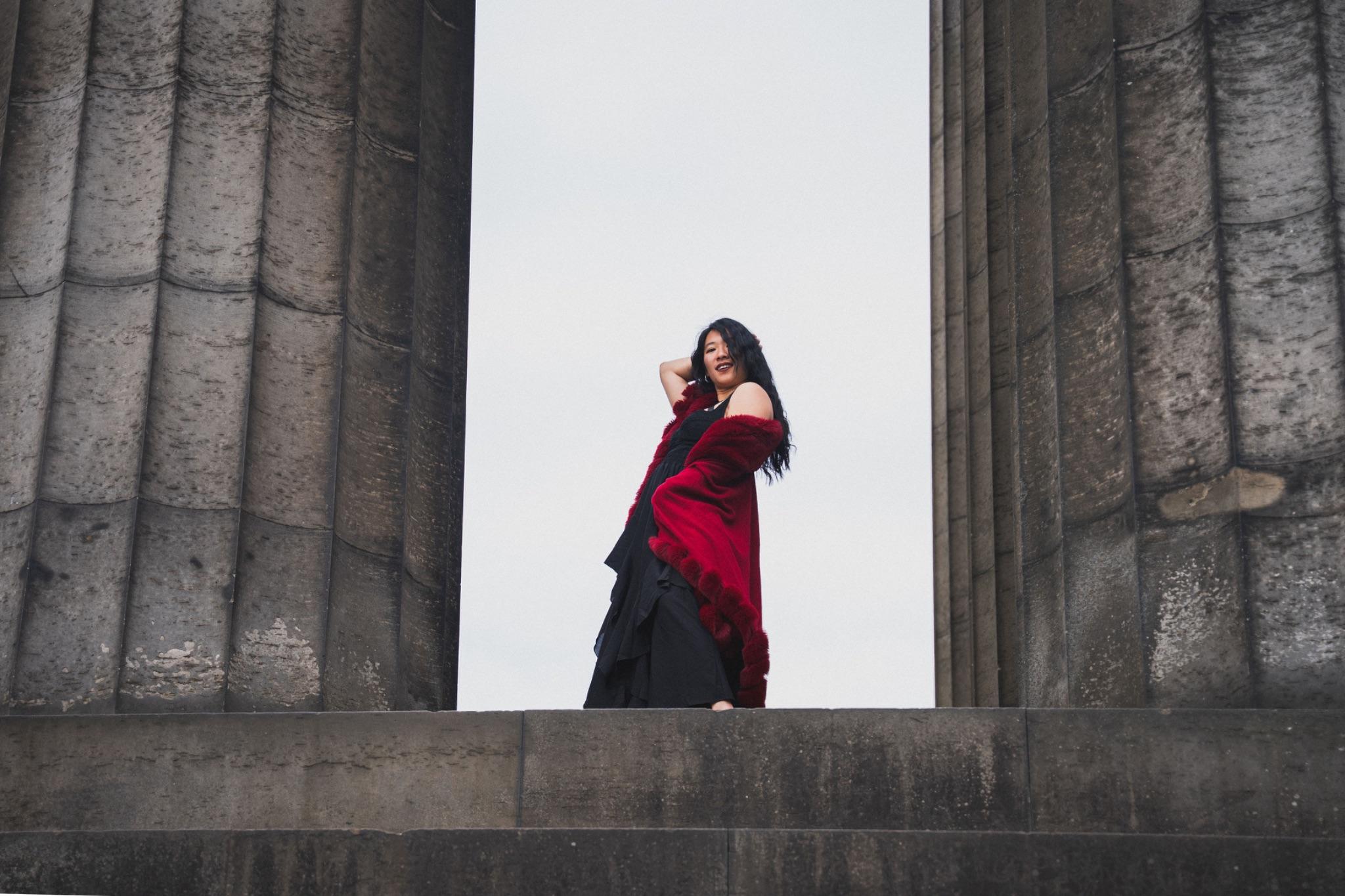 Mistress Mahara in a red cape between tall stone columns
