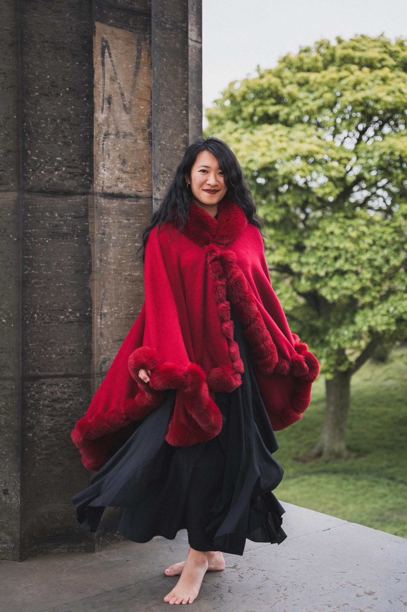 Mistress Mahara walking in a red cape past stone columns