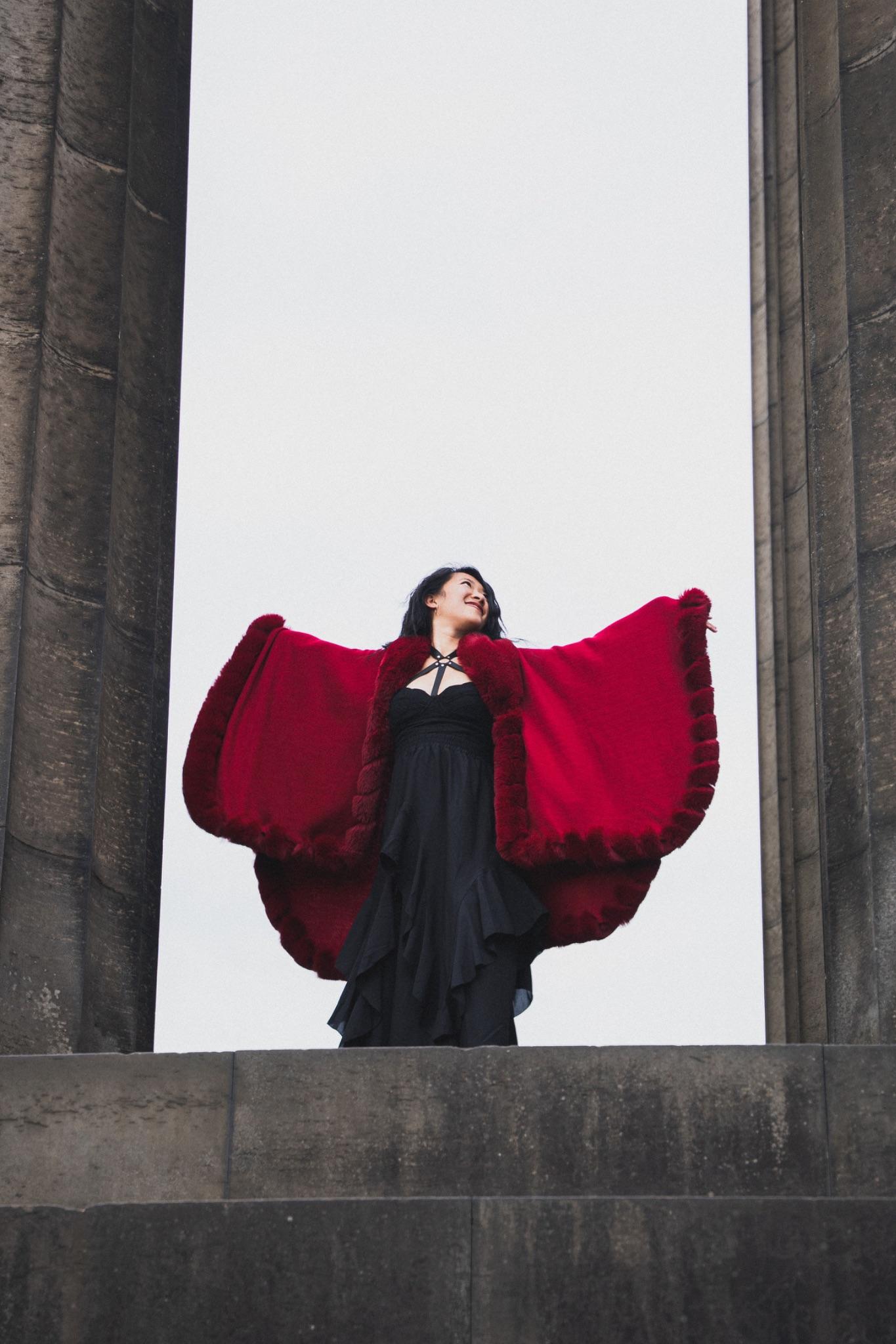 Mistress Mahara in a red fur cape, arms outstretched between two stone temple columns