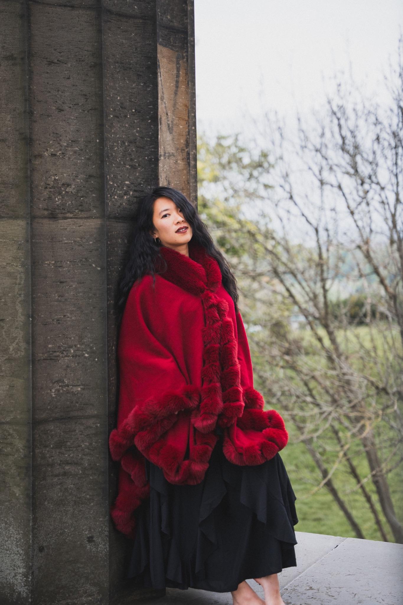 Mistress Mahara in a red cape leaning against a stone column