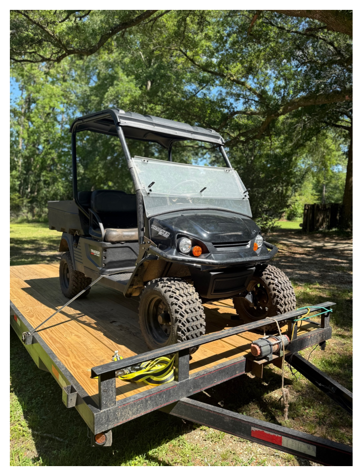 Black golf cart loaded on a wooden-deck equipment trailer outdoors