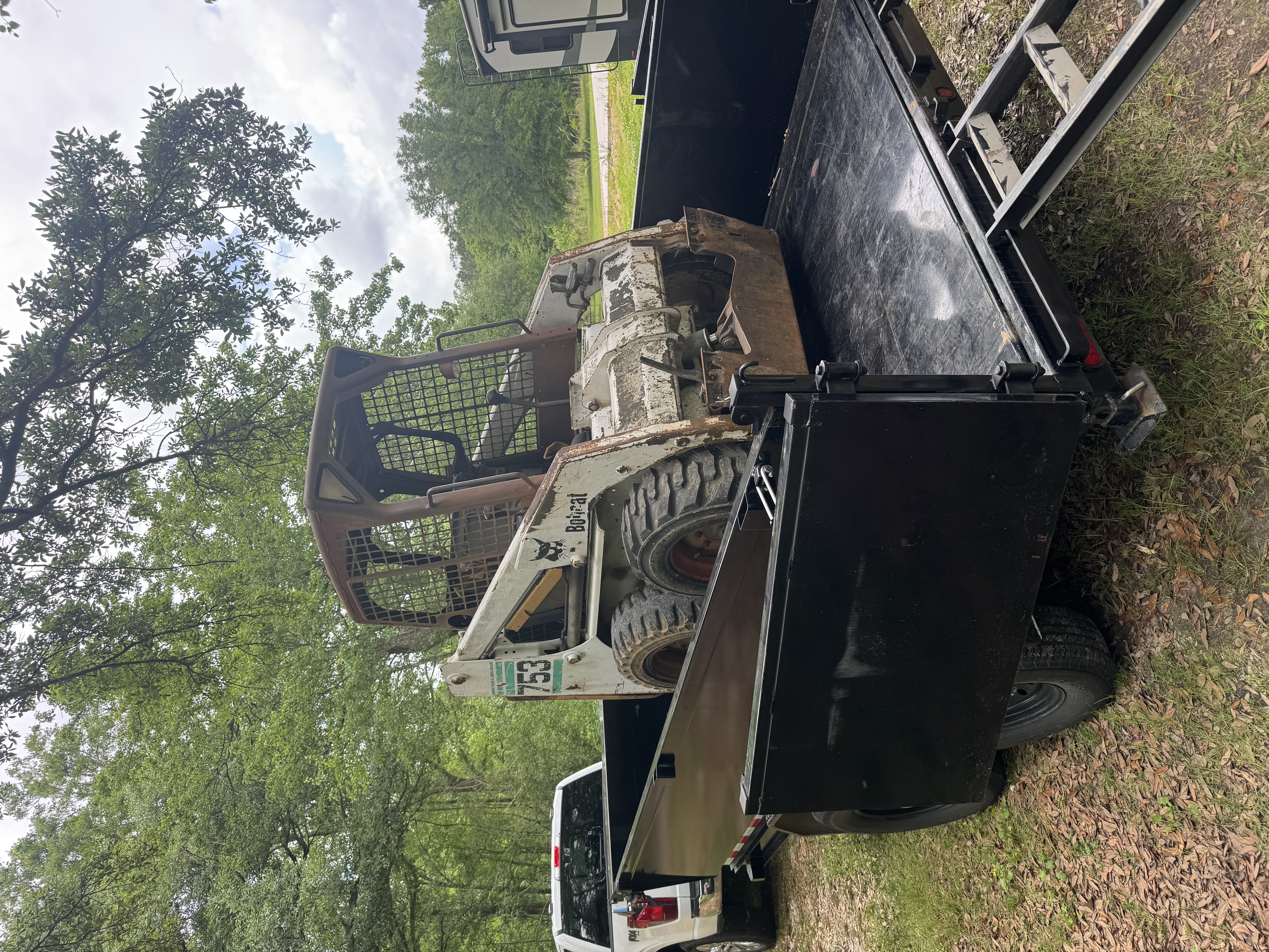 Used Bobcat 753 skid steer loaded on a black trailer behind a pickup truck