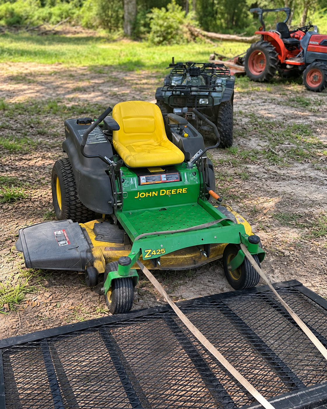 John Deere Z425 zero-turn mower beside a trailer ramp during an equipment pickup