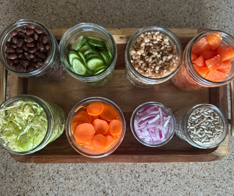 Prepped ingredients in jars for citrus avocado winter salad including greens, vegetables, and toppings