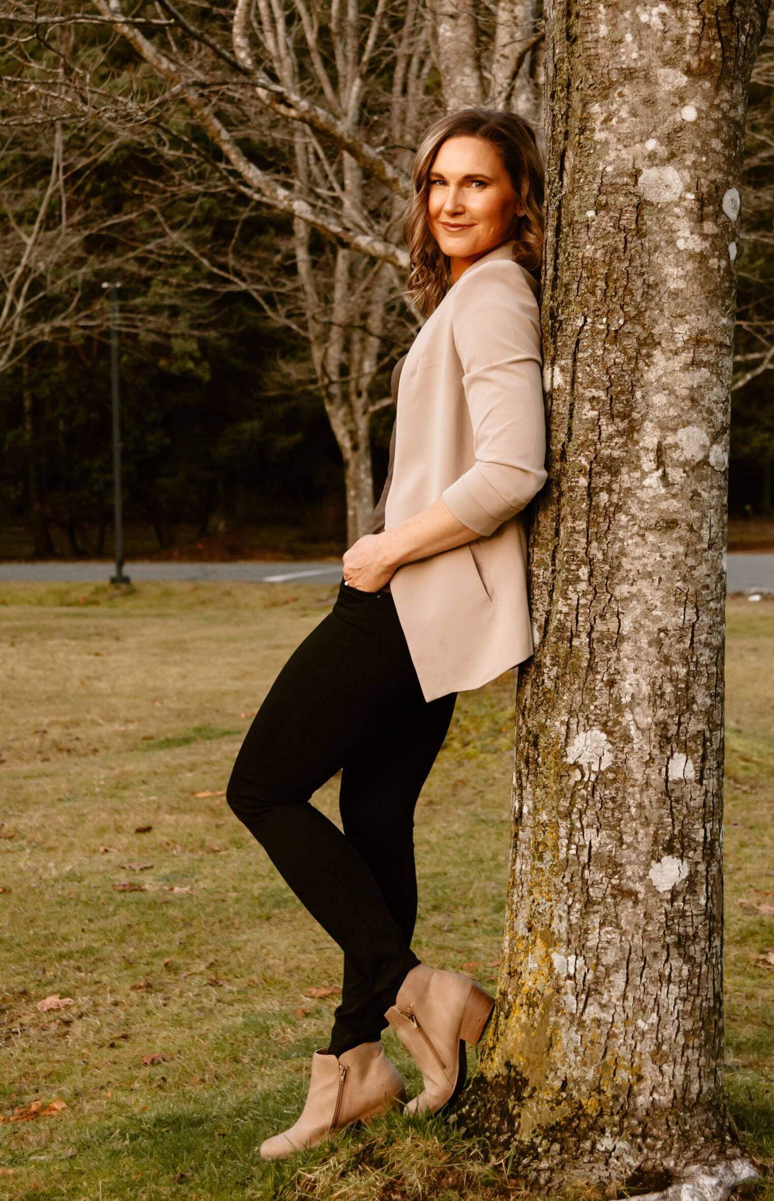 Linda Bartholme leaning against a tree outdoors, providing midlife transformation and resilience life coaching for women.