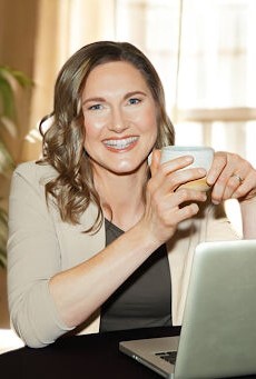 Workplace wellness coach Linda Bartholme smiling with a tea cup and laptop, demonstrating balanced productivity.