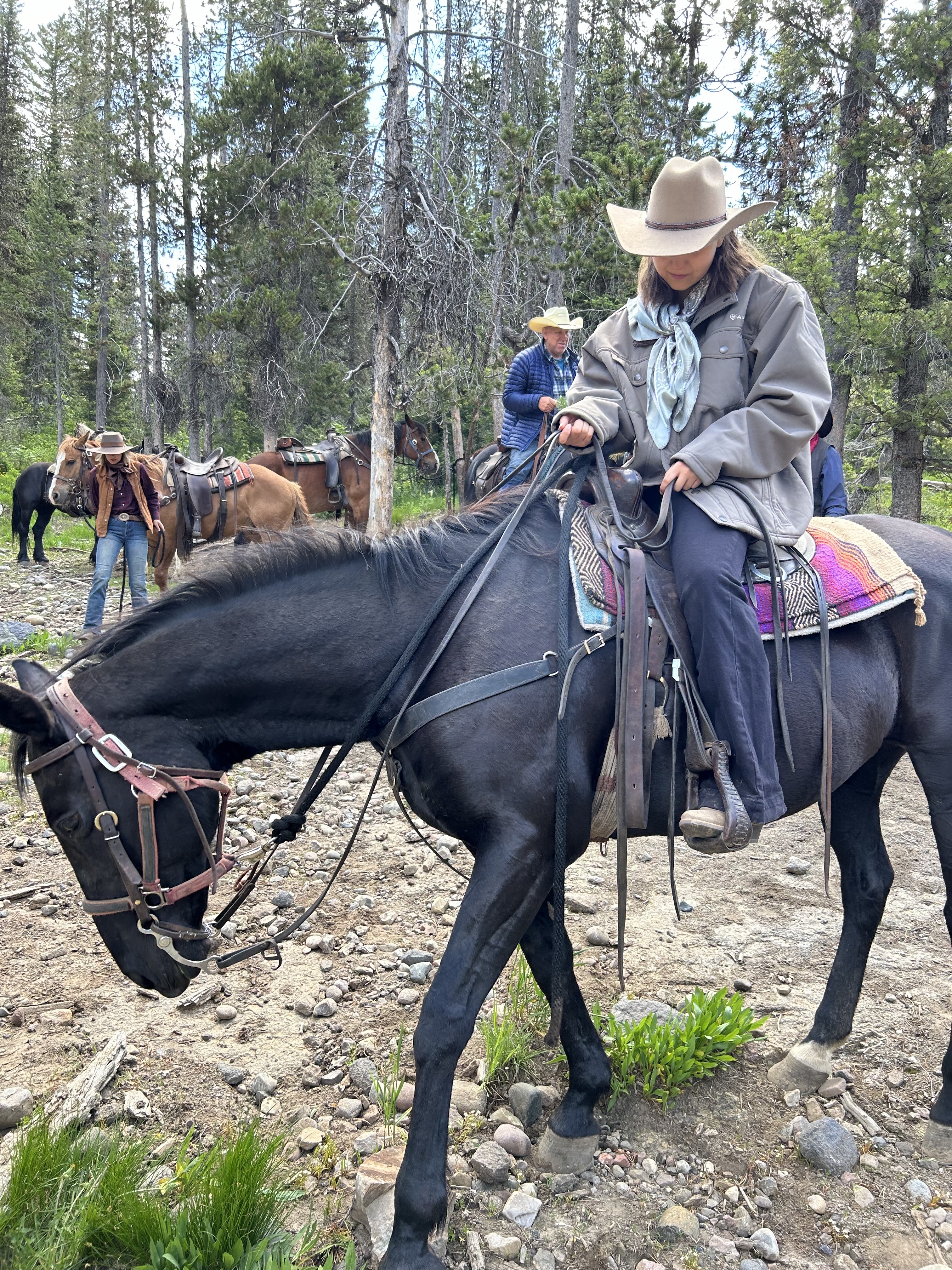 A young rider wearing a custom Hangman Hats hat on horseback on a wooded trail