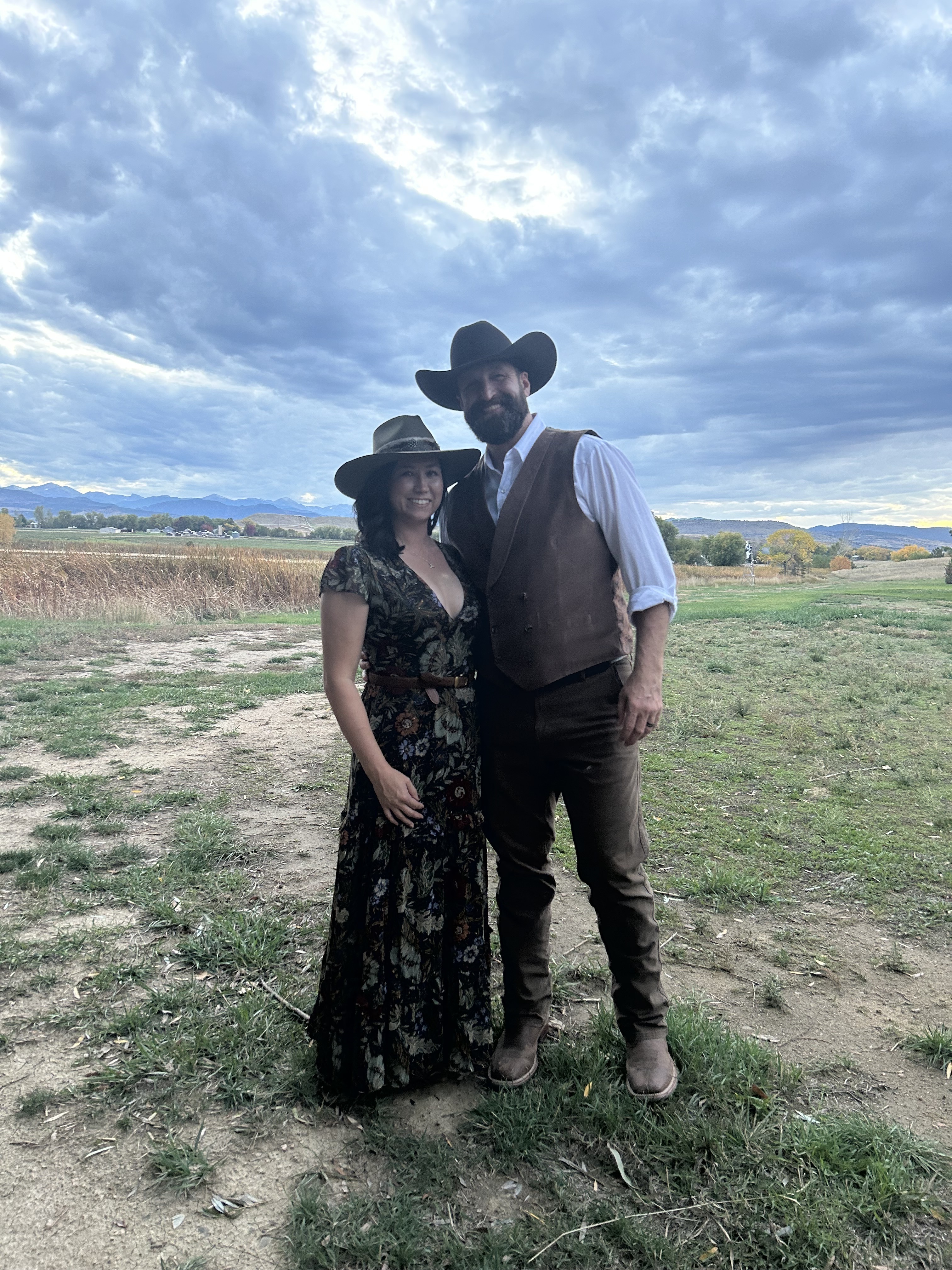Justin and Jen, the founders of Hangman Hats, standing together in a field wearing custom hats