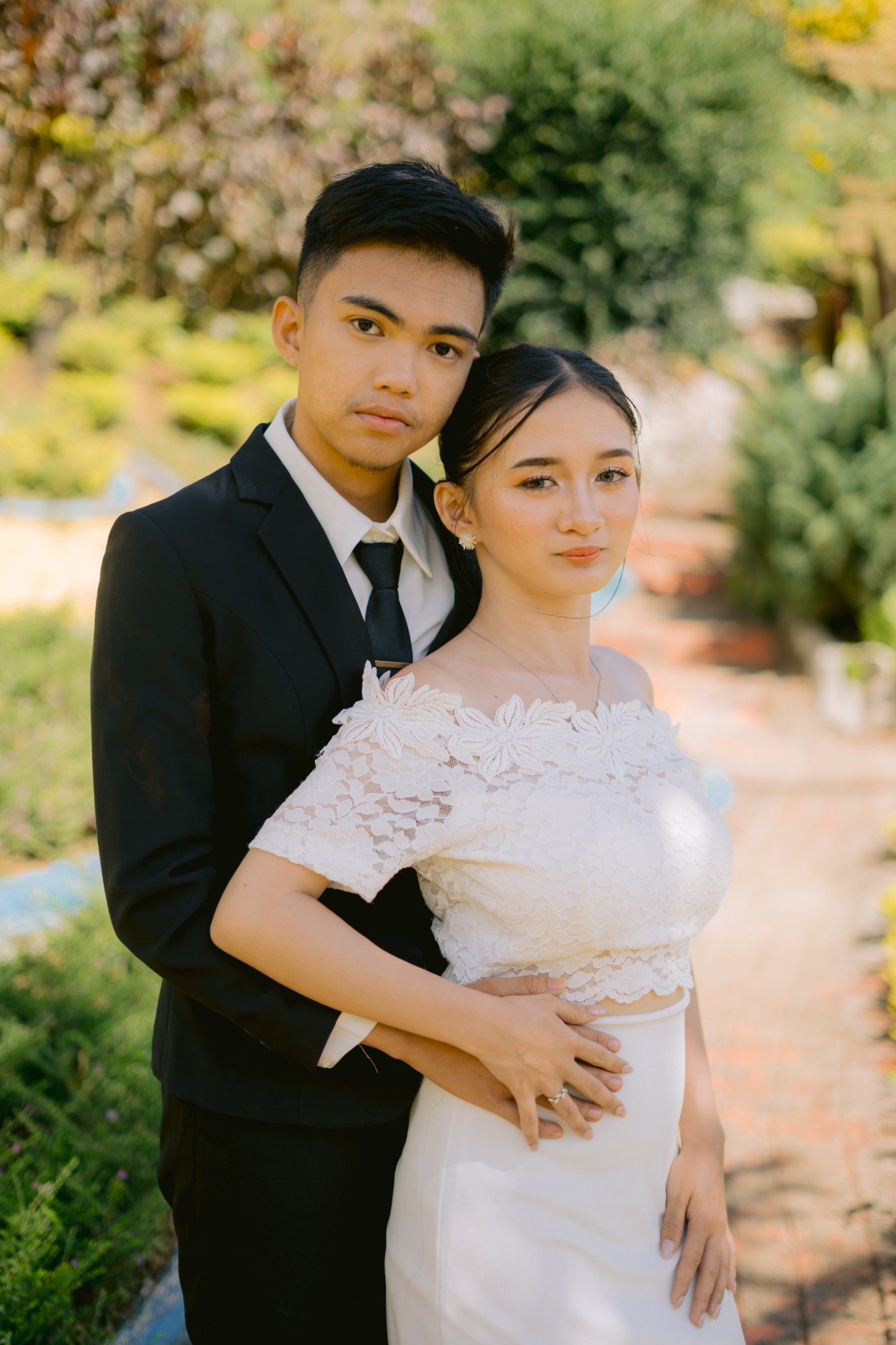 The bride and groom in a close embrace in a sunlit garden, looking at the camera