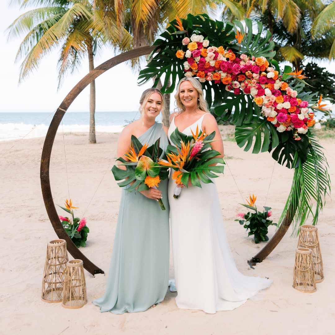 Pareja celebrando su boda en la playa con arco floral tropical