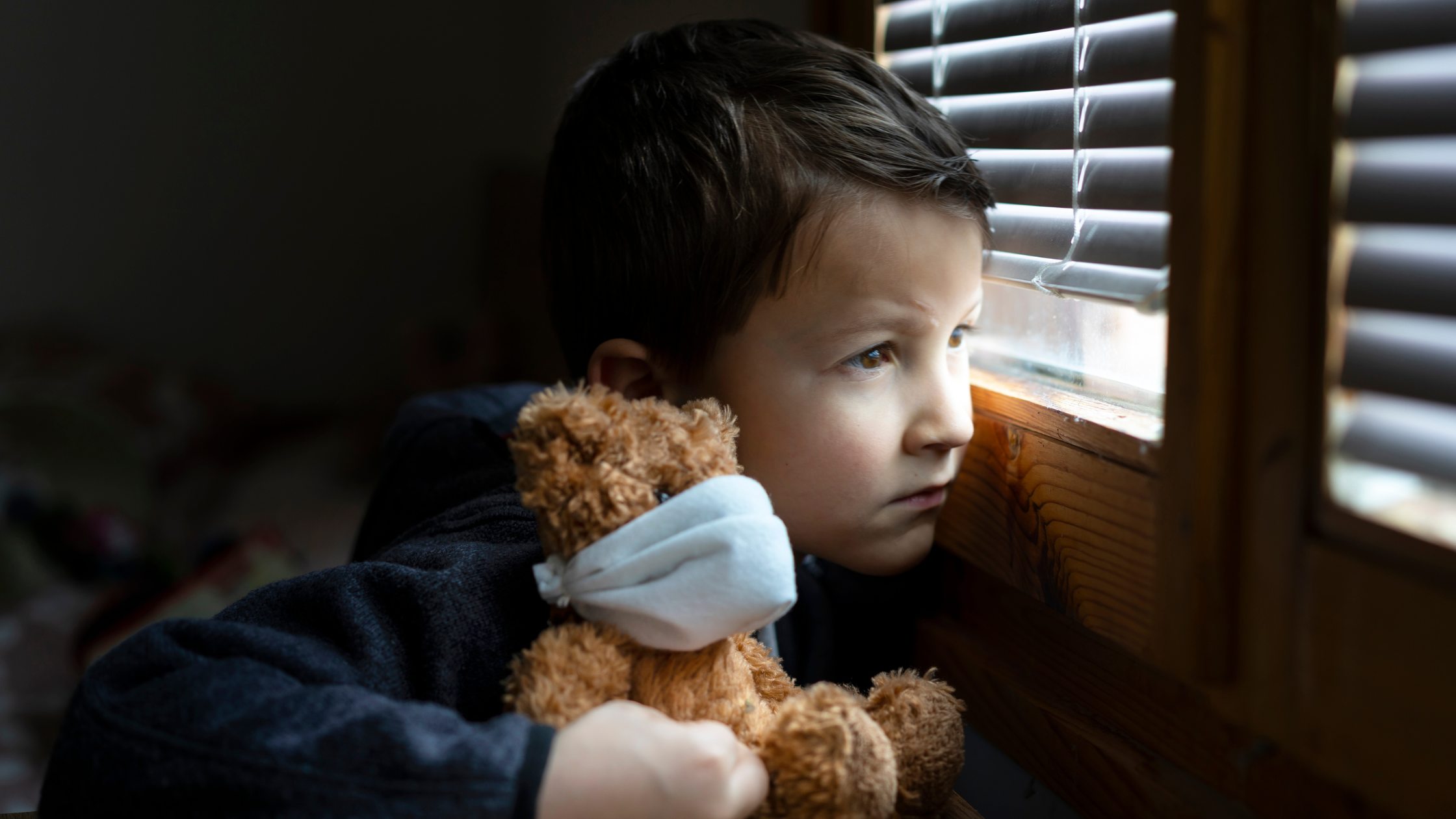 Child holding teddy bear looking withdrawn at window, representing childhood trauma, emotional neglect, parental dysfunction, and how childhood wounds create narcissistic personality development