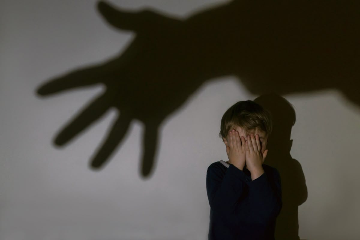 Child covering face in fear with threatening shadow looming, representing child abuse, narcissistic parenting, generational trauma, and how narcissistic parents psychologically harm children