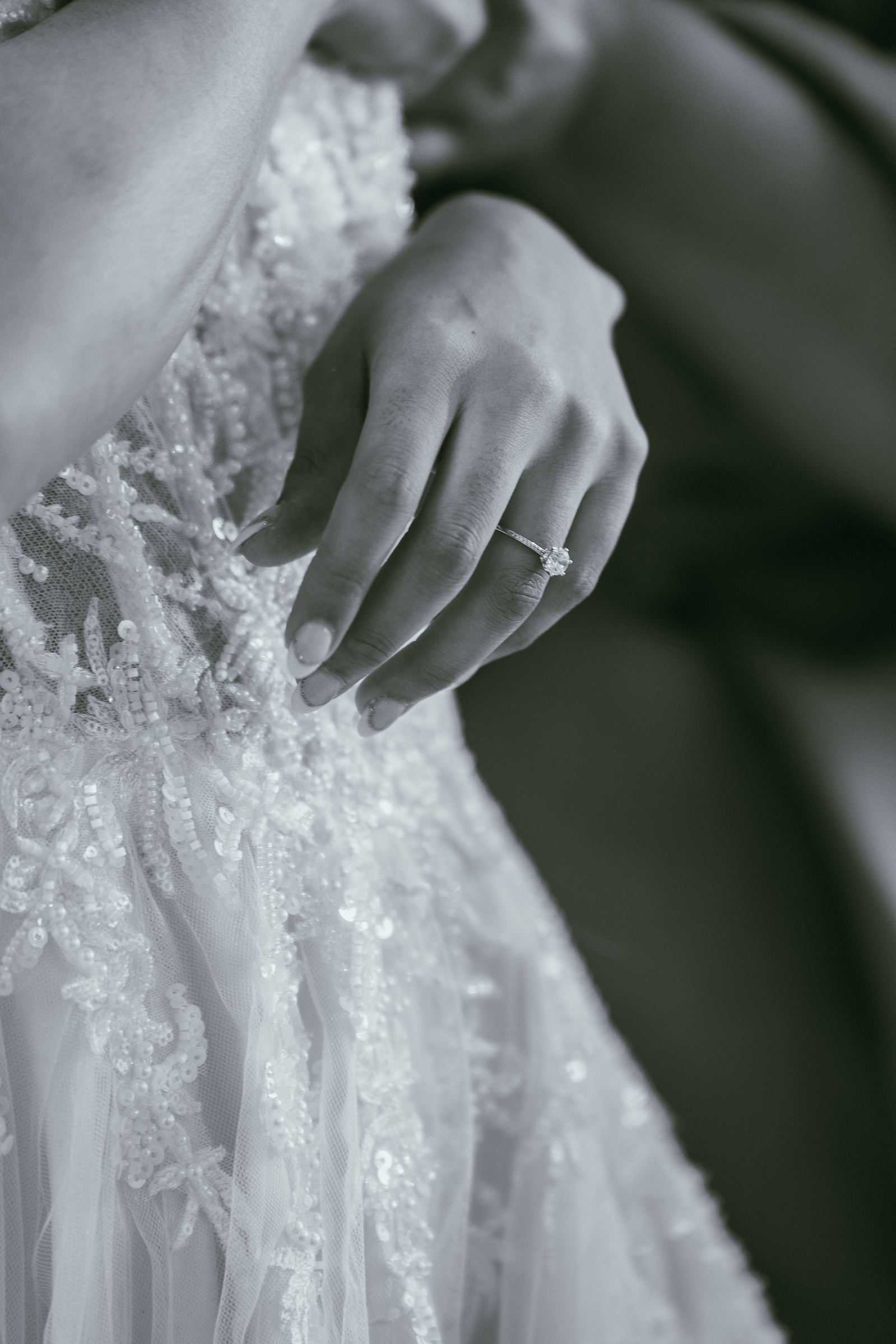 A groom’s hand on the bride’s lace gown, in black and white