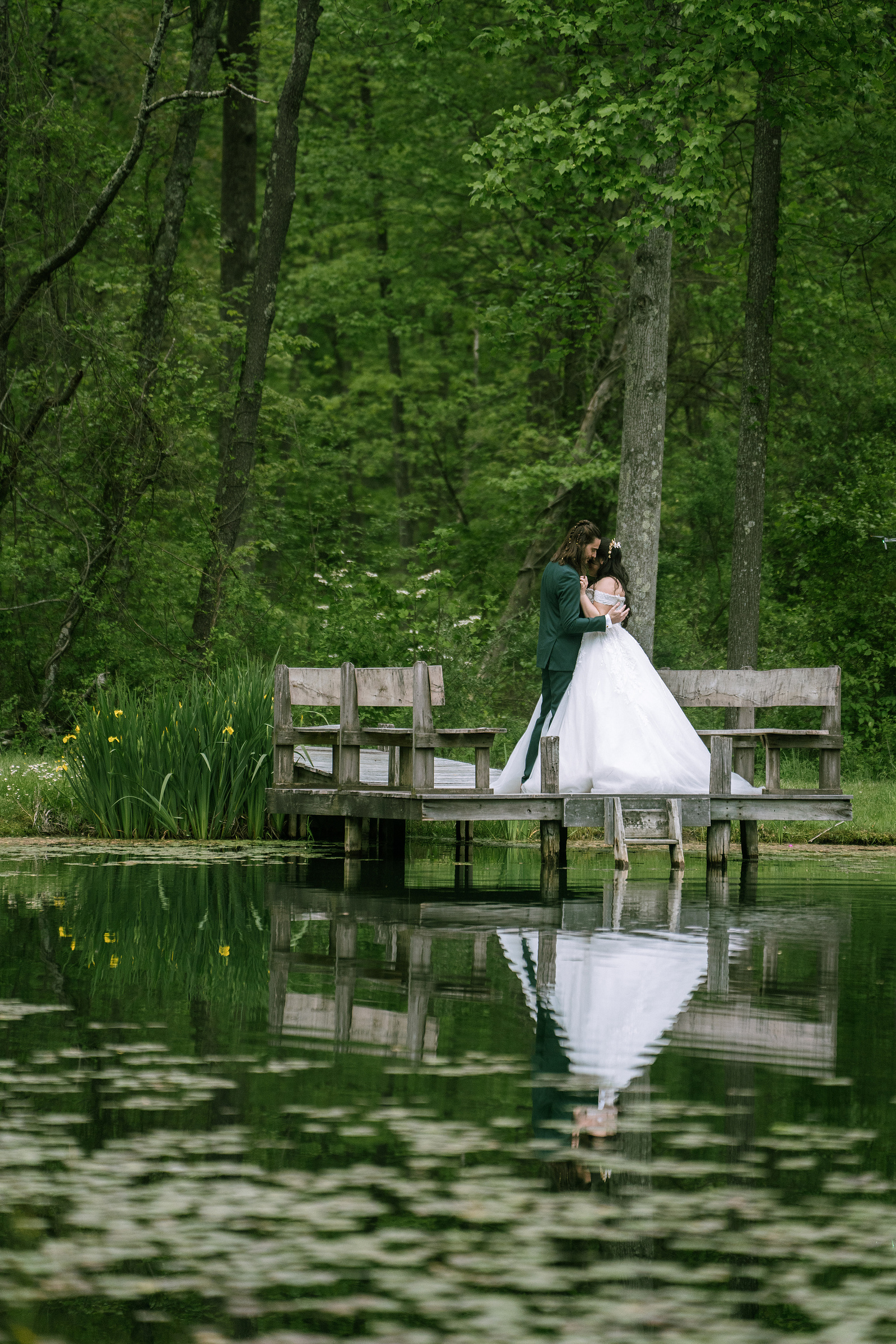 A bride standing on a wooden dock by a woodland pond on her wedding day