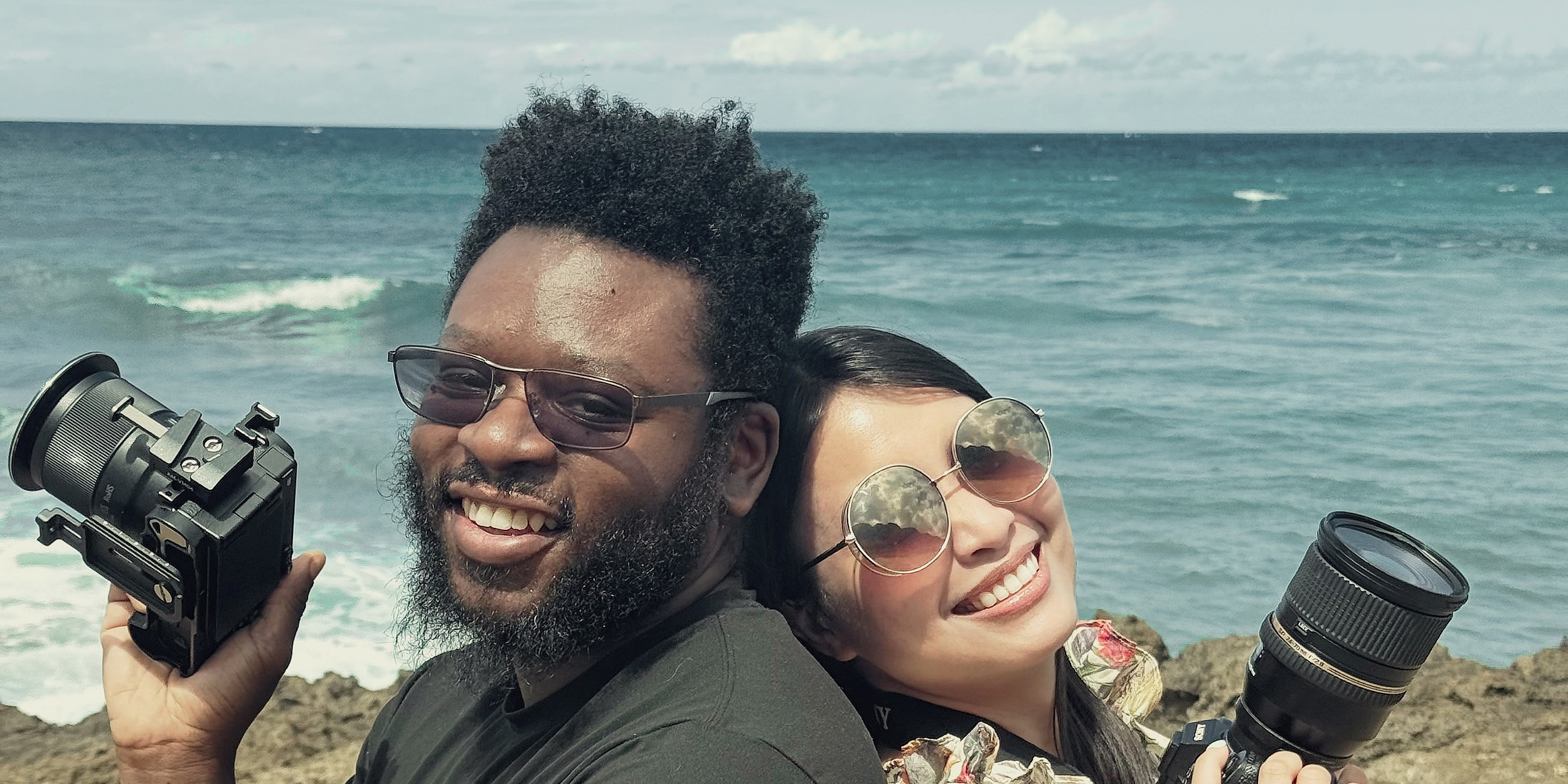 Rezia Braza and Jamal Mortimer of RedJam Production by the ocean, each holding a camera